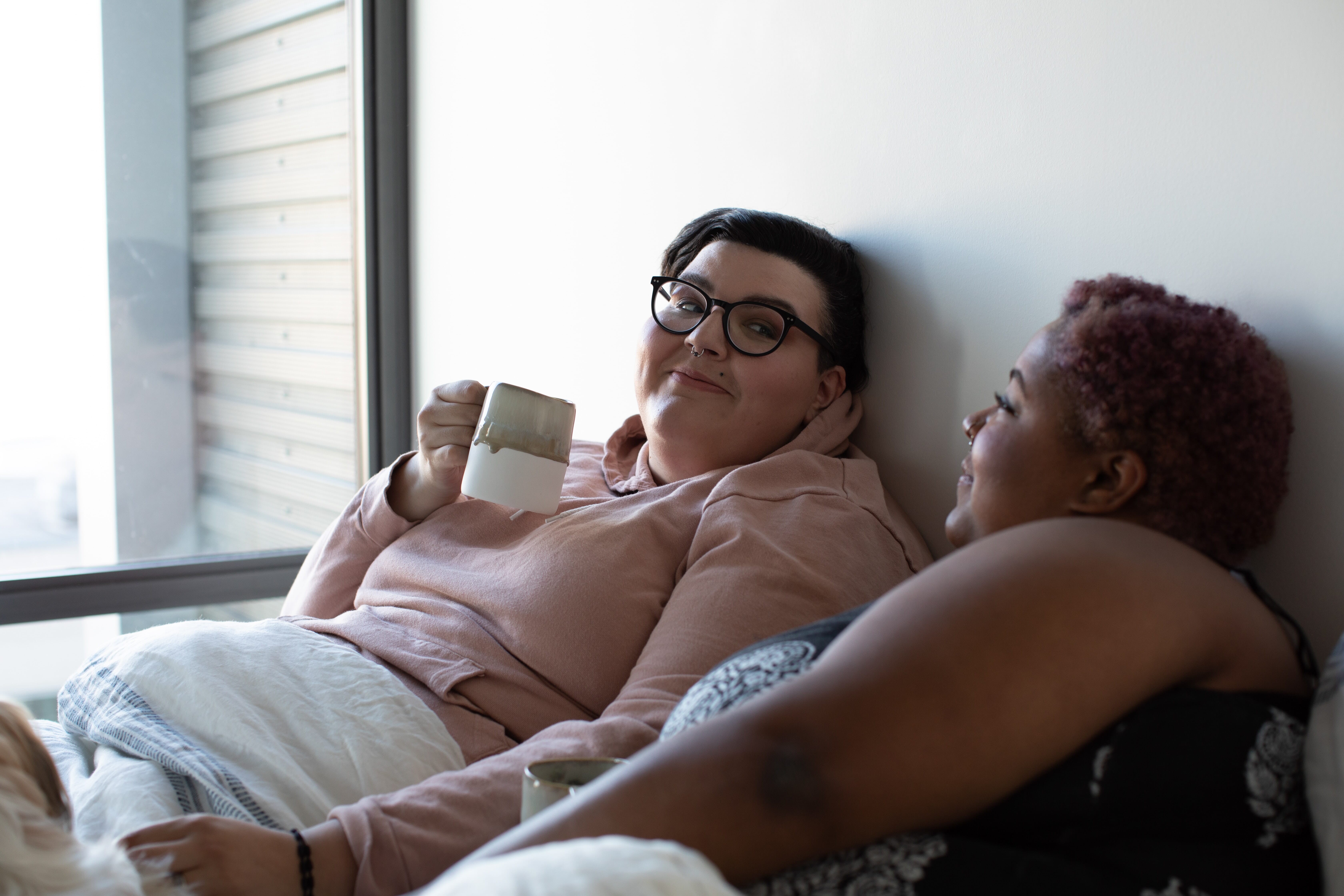 lesbian couple talking and drinking coffee in bed