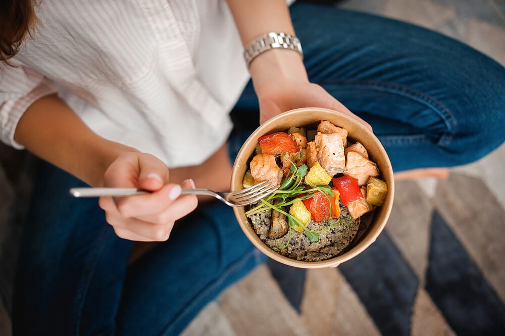 woman sitting cross-legged eating a healthy meal in a bowl