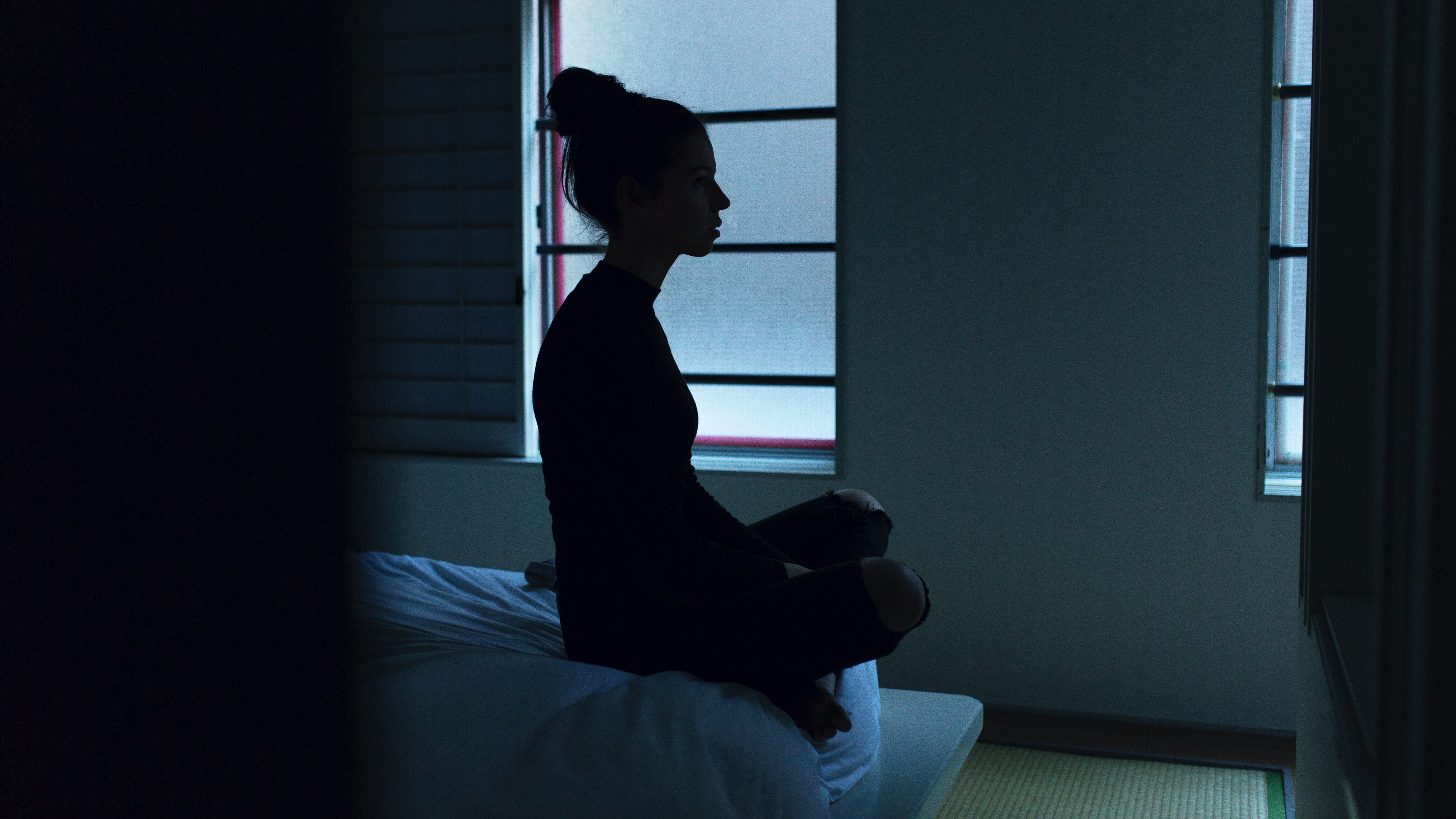 woman sitting at the edge of a bed in a dark room