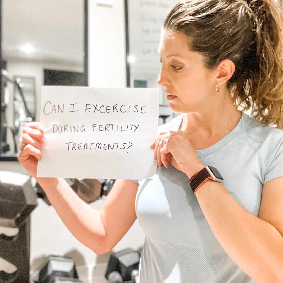 woman holding a sign that reads "can i exercise during fertility treatments"