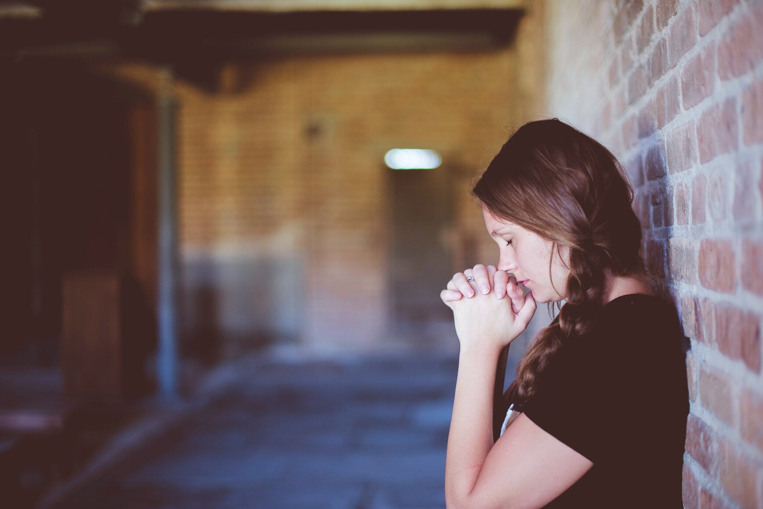 woman against a brick wall eyes closed, praying