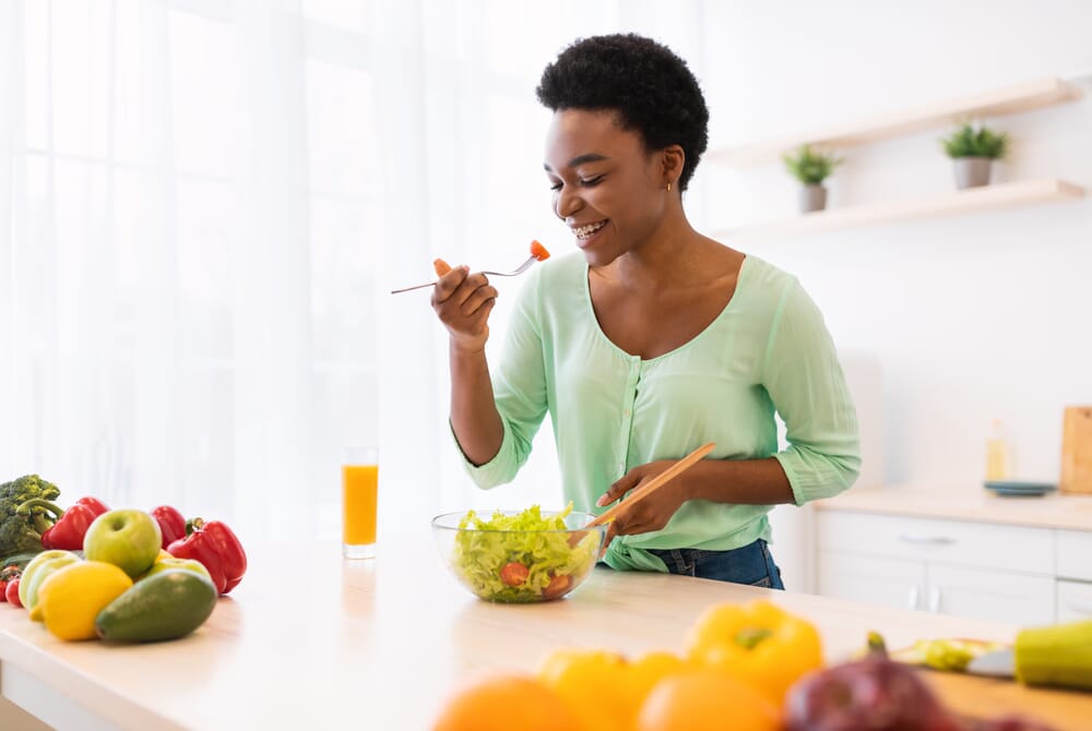woman standing at kitchen island eating a healthy salad