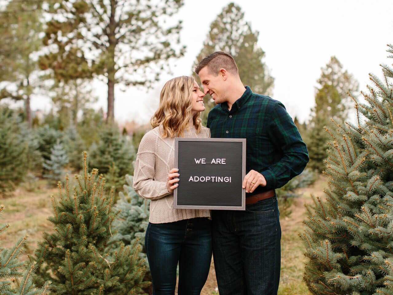 infertility warrior jen lowell and her husband holding a sign that reads &quot;we are adopting&quot;