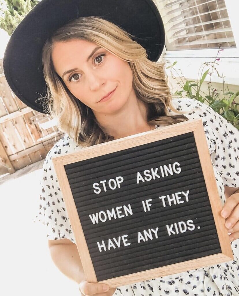 millie brooks holding a sign that reads stop asking women if they have kids