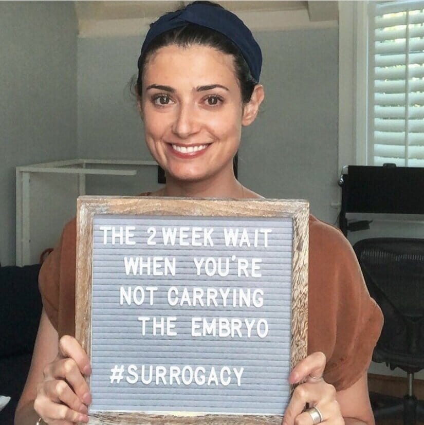 woman holding sign about the two week wait with a gestational surrogate