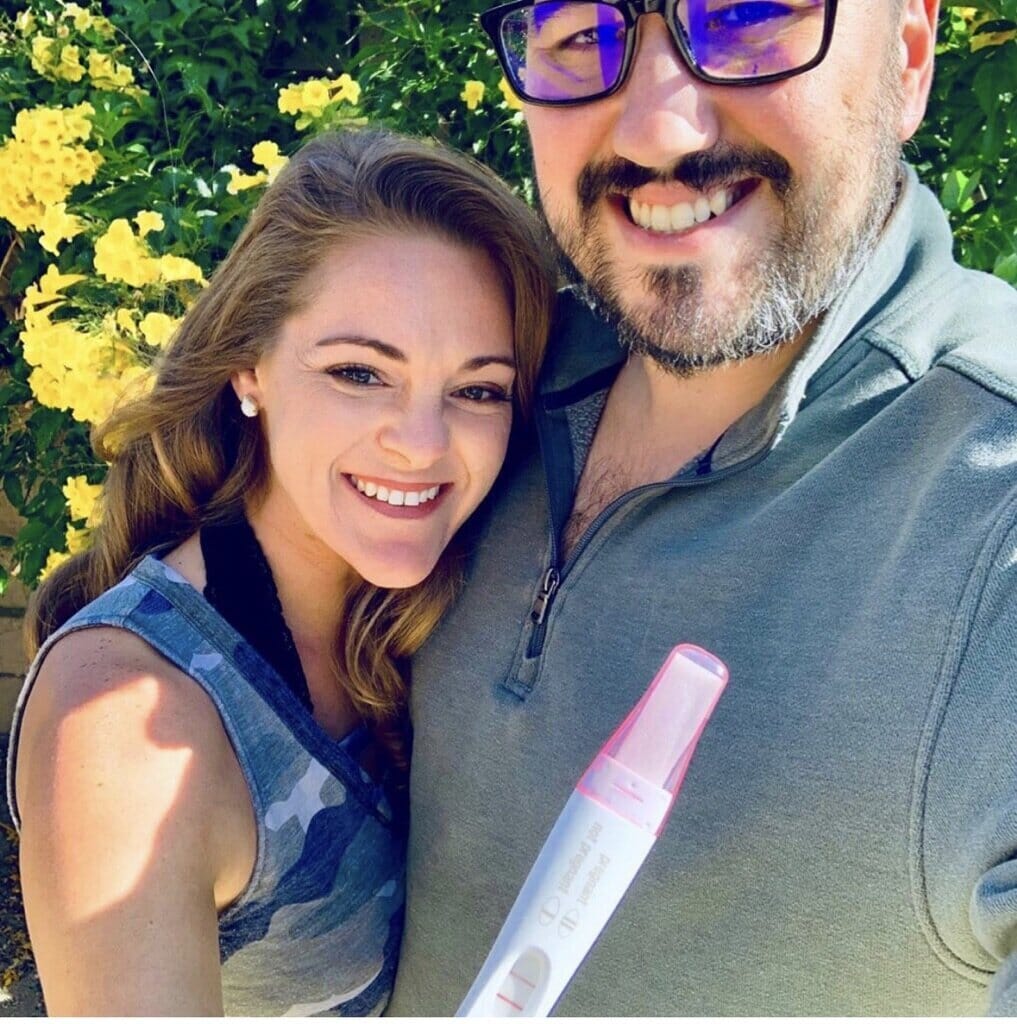 infertility warrior emily attenhofer with her husband and a positive pregnancy test