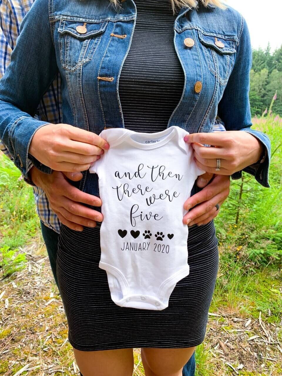 woman holding baby onesie that reads &quot;and then there were five&quot;