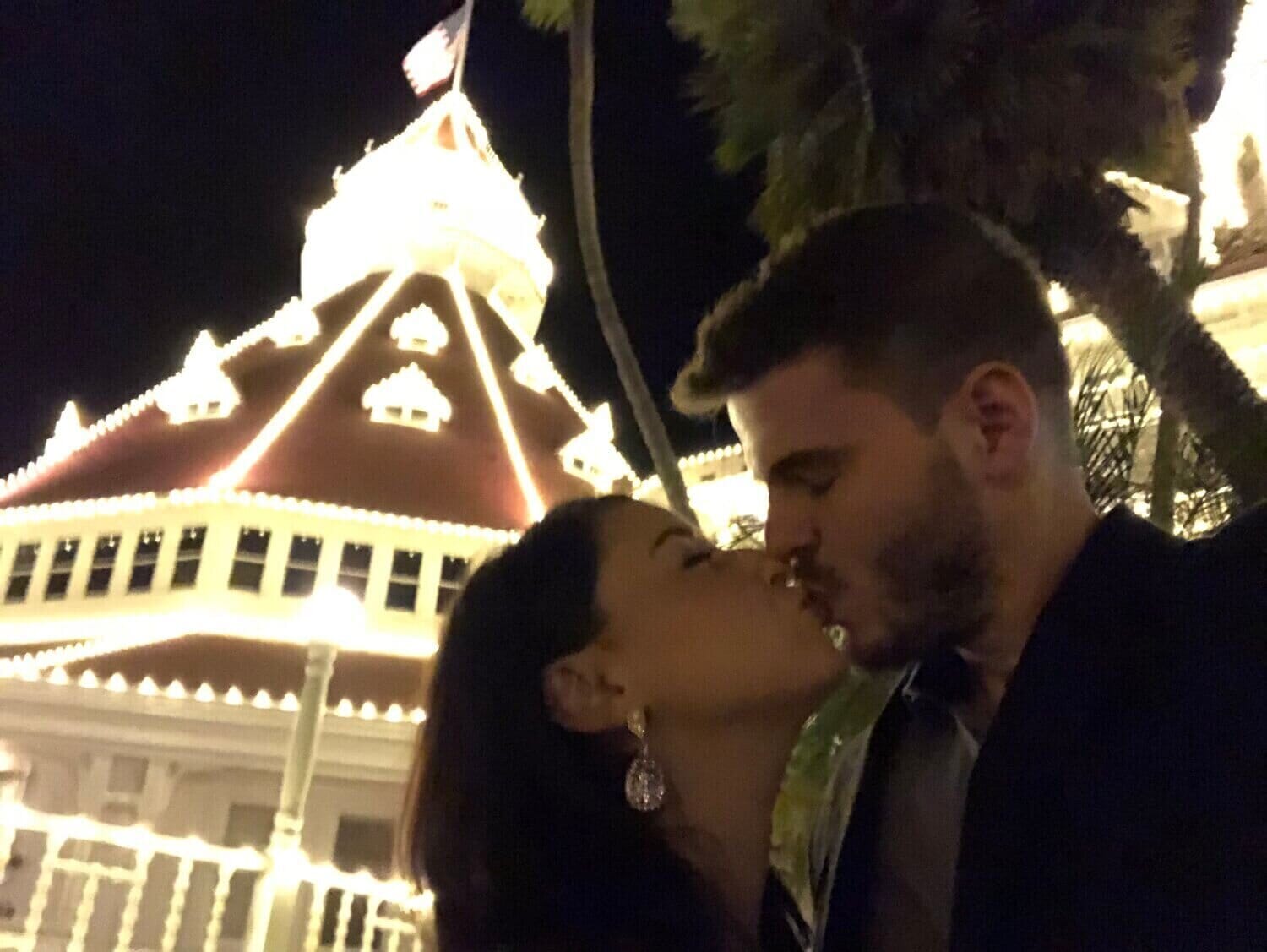 woman and man kissing in front of holiday lights